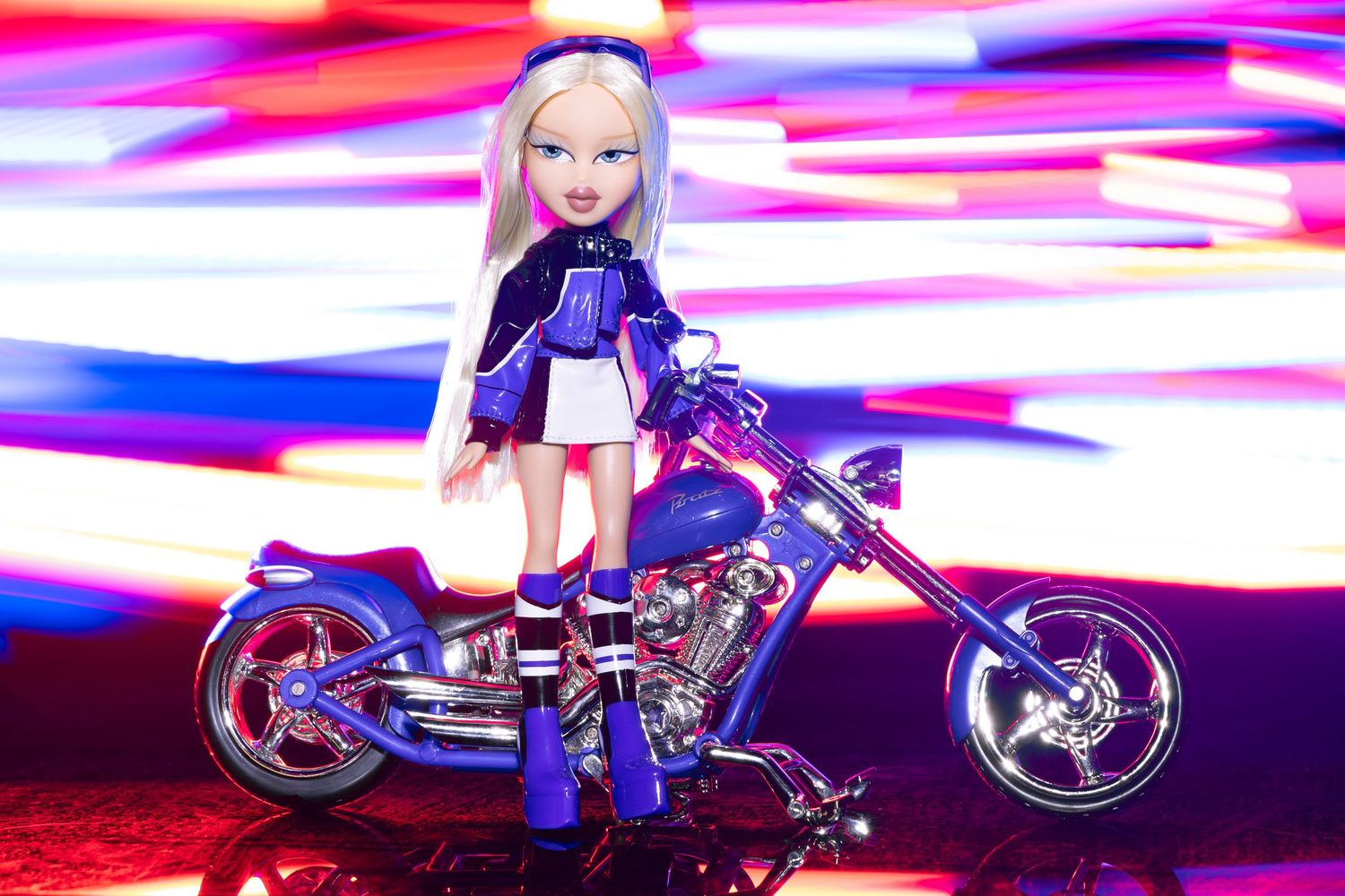 Bratz doll with blonde hair posed on a purple chopper motorcycle against a vibrant neon light background.