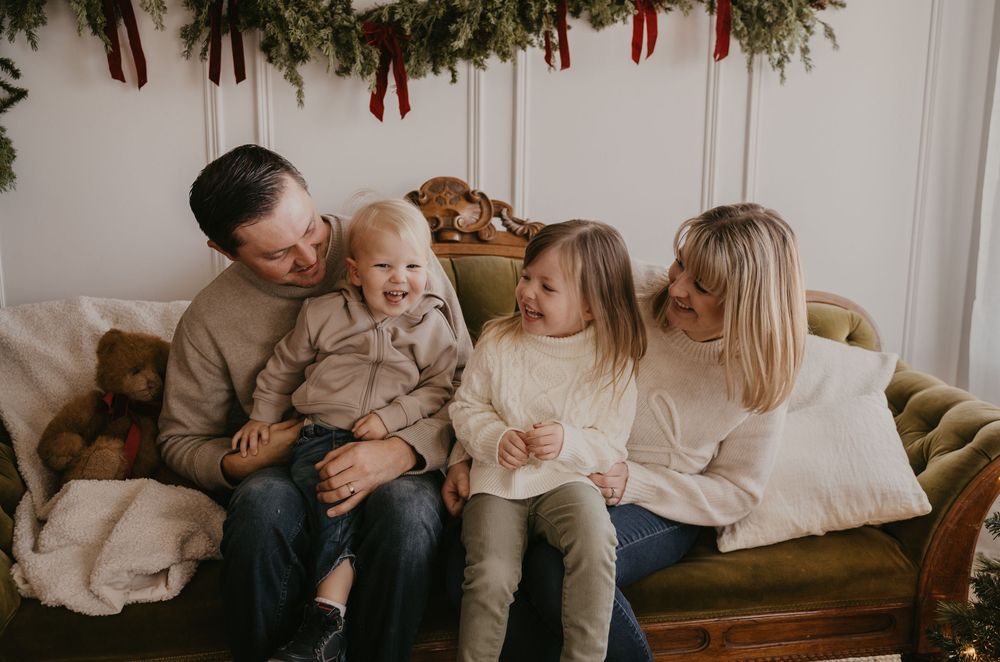 Family lounges together on a cozy cream-colored couch during an intimate indoor photo session.