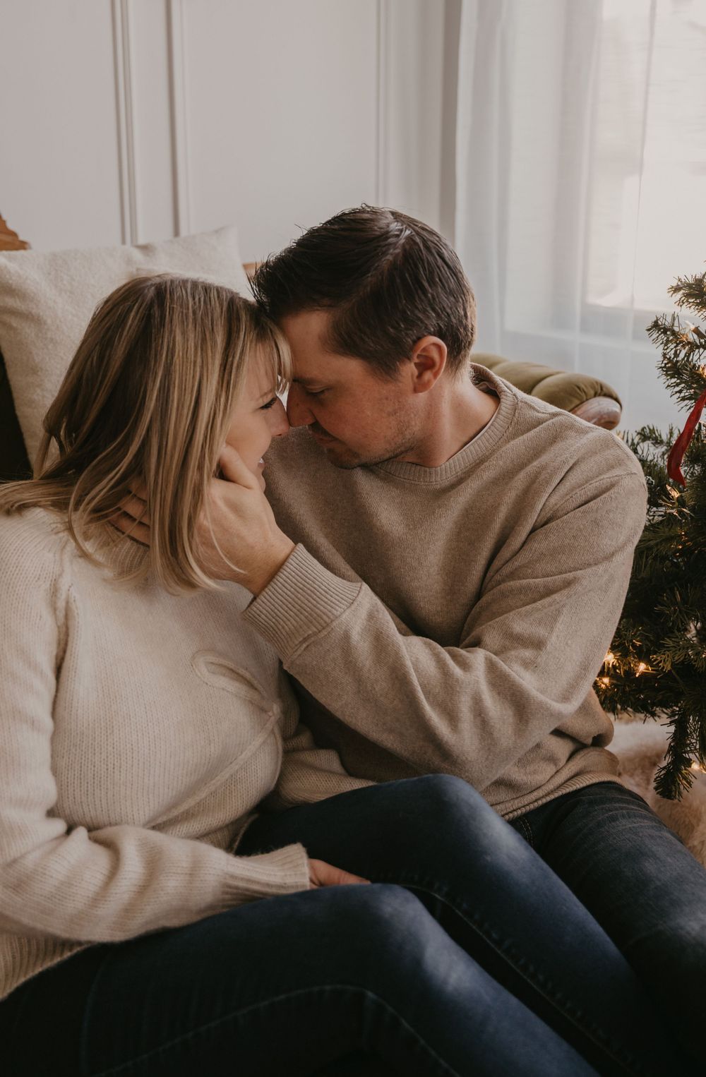 A romantic couple in neutral sweaters sharing intimate moments on a couch in a softly lit room.