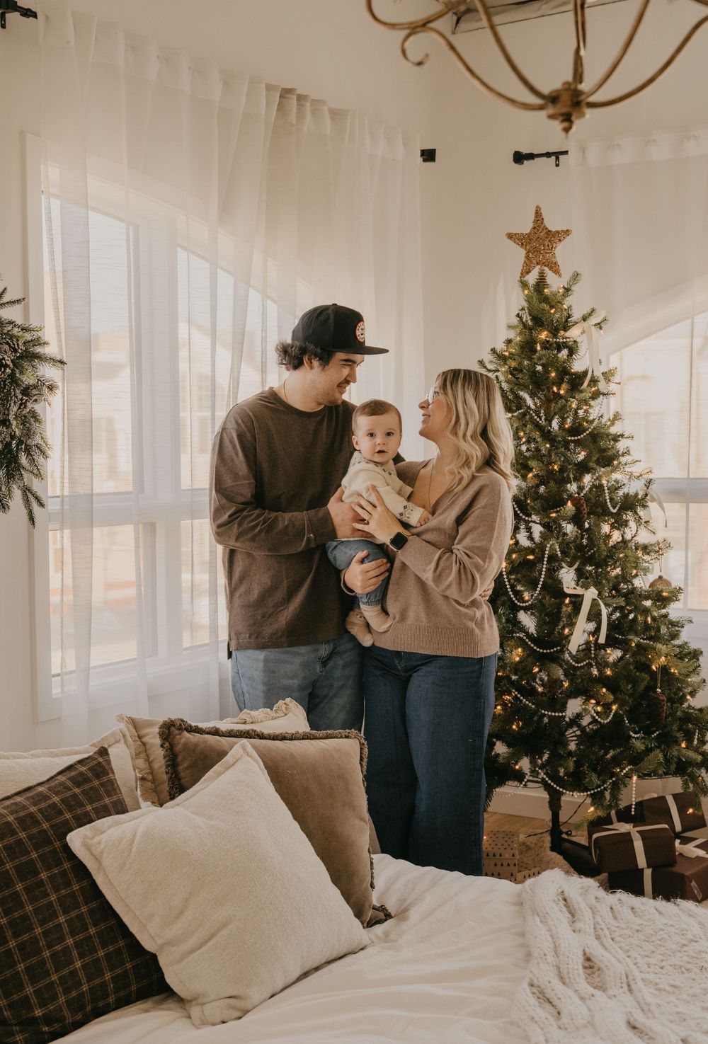 A family shares a tender moment by their decorated Christmas tree in a bright, airy living room.