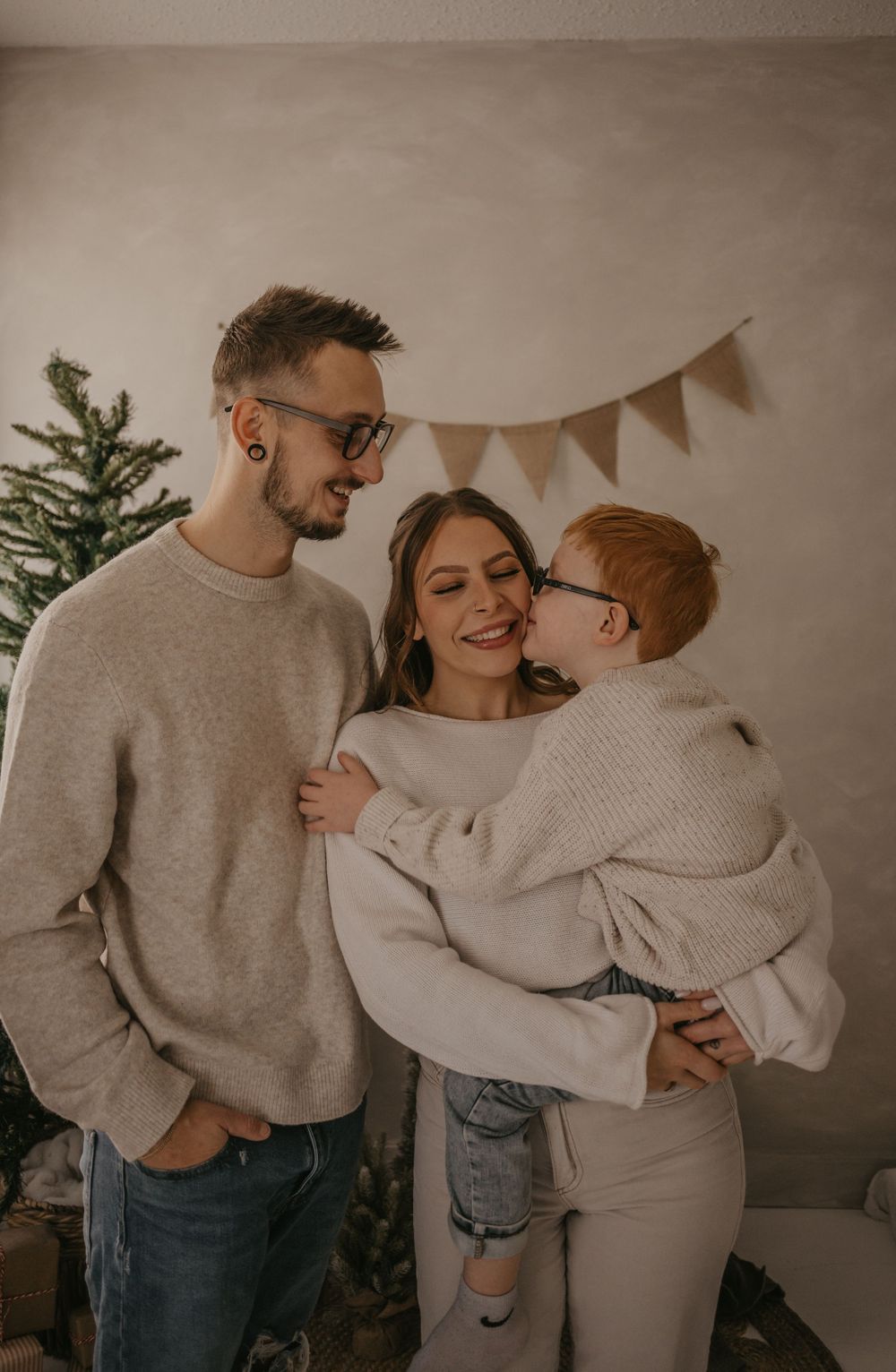 Family in matching beige sweaters sharing tender moments together in a cozy room with holiday decorations.