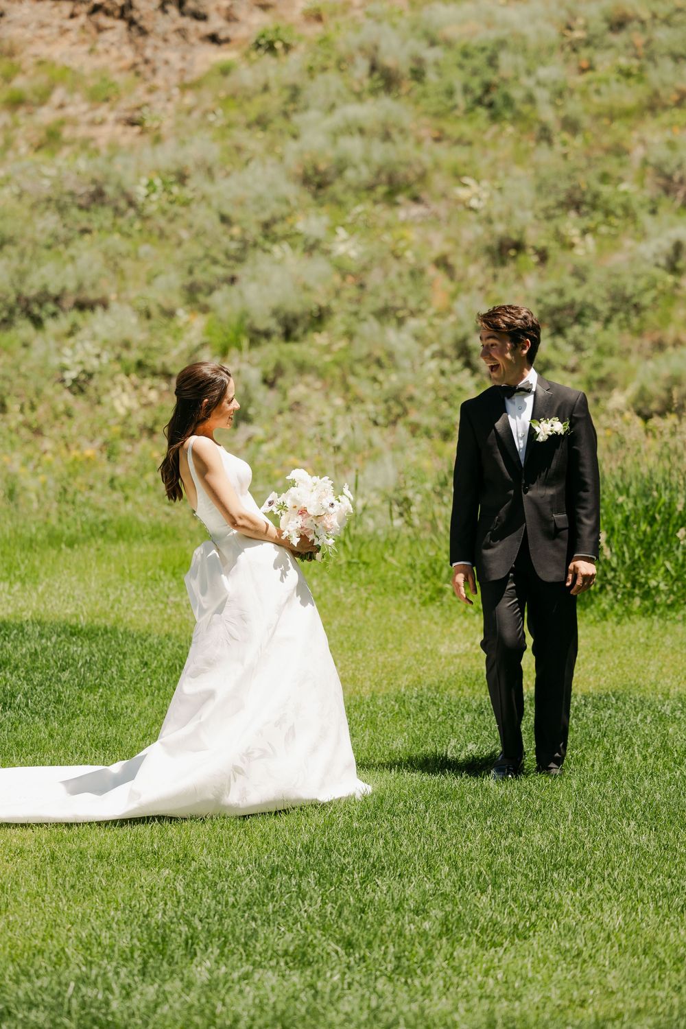 Wedding couple playfully posing on a grassy hillside in formal attire.