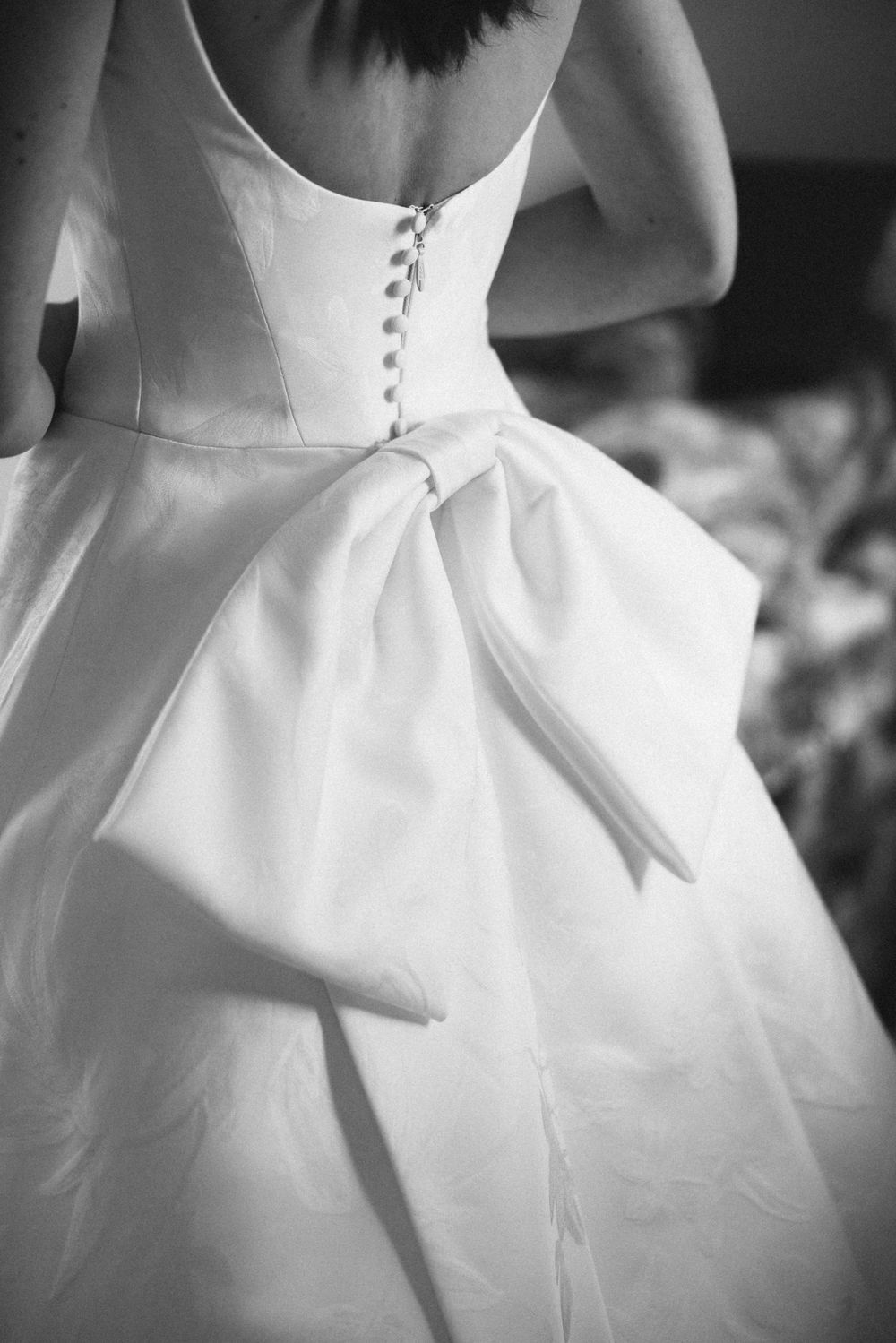 Close-up details of white wedding dresses with buttons and bows shown in black and white photography.