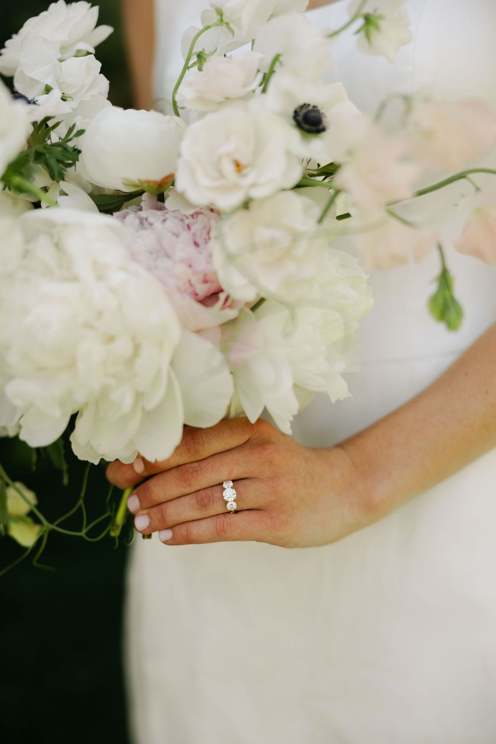 White peonies and flowers held in hands with an engagement ring sparkling in natural light.