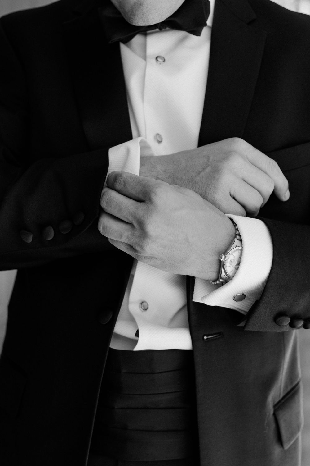 Close-up of hands adjusting cufflinks on a formal black tuxedo with white dress shirt and bow tie.