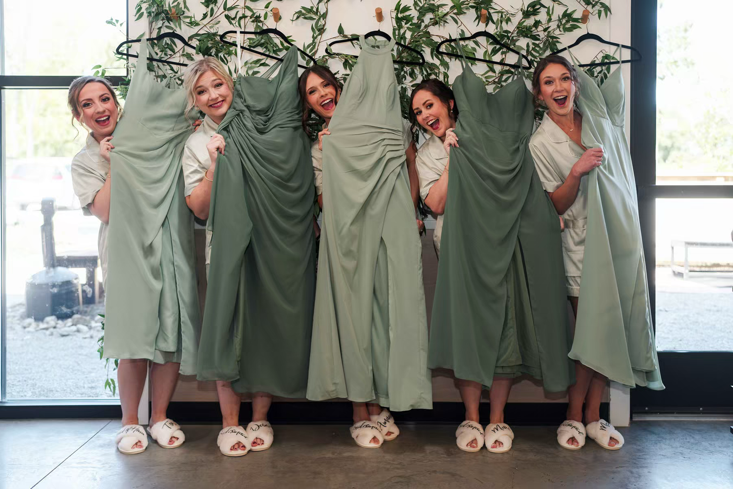 A group of bridesmaids in sage green dresses pose together showing off their matching sandals in Retreat 21 Wedding Venue