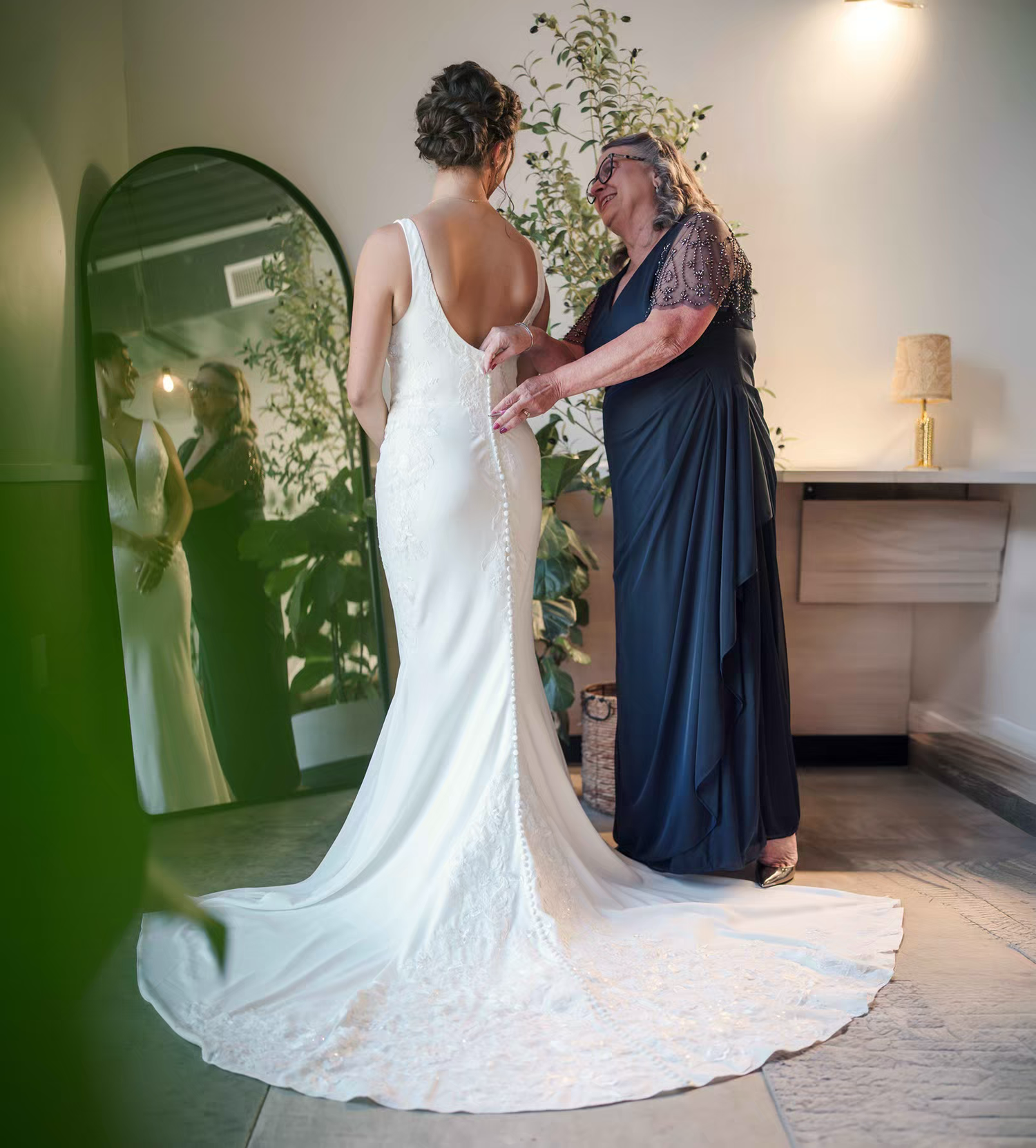 A mom in a navy blue dress helps adjust the long white wedding gown train of her daughter in Retreat 21 Wedding Venue