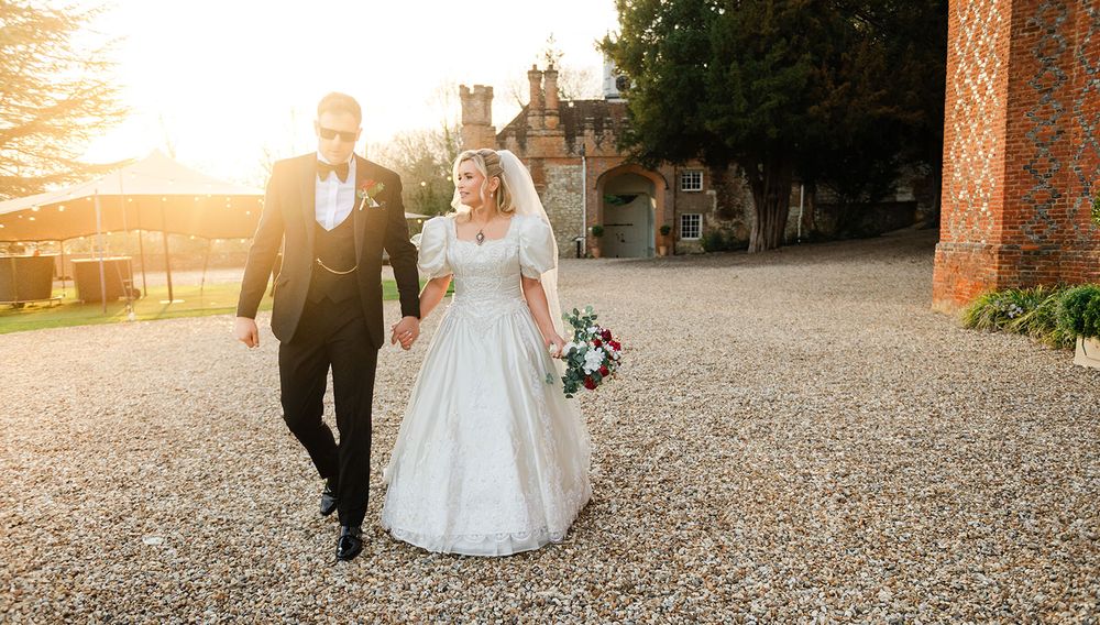A couple walks hand in hand down a gravel path during sunset at a romantic outdoor venue.