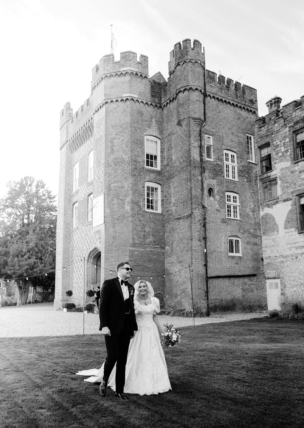 A black and white photo series showing a couple posing outside a grand medieval castle with crenellated towers and walls.
