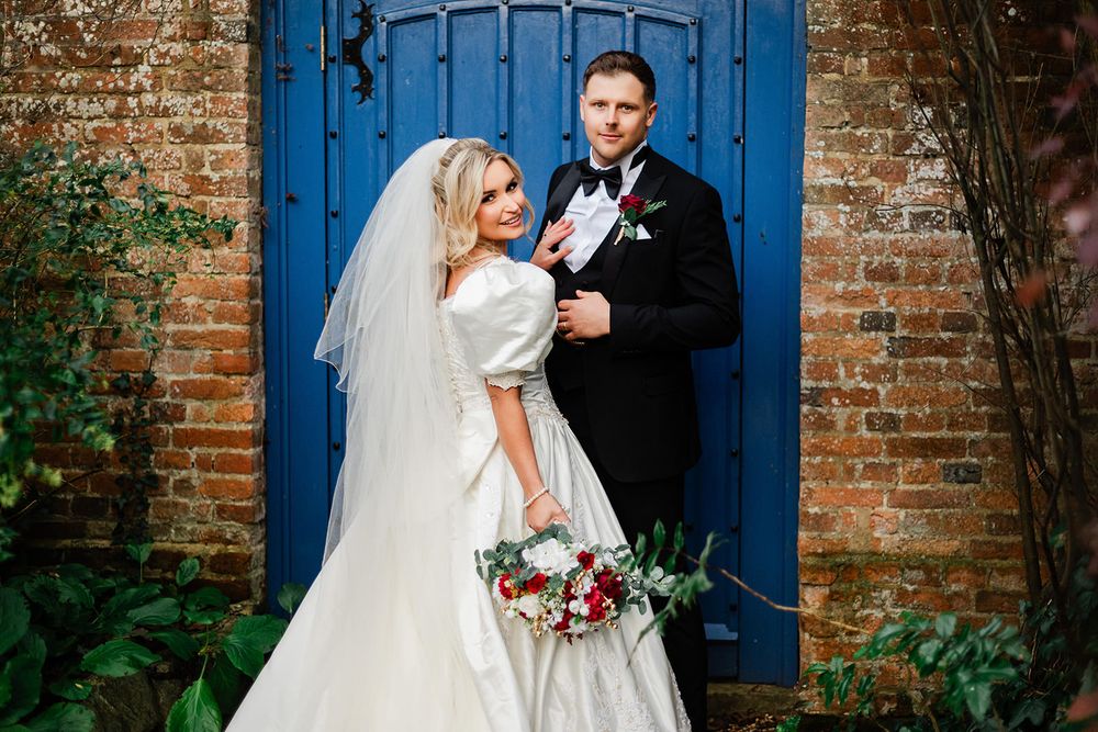 A bride and groom share romantic moments in front of a rustic brick wall with bright blue doors.