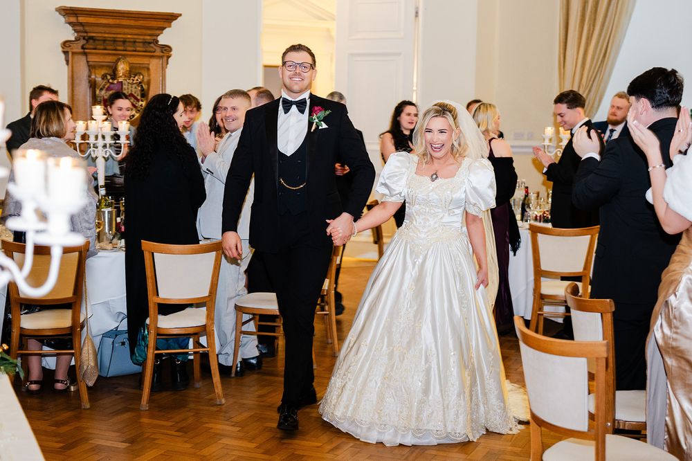 Wedding reception guests in formal attire dancing and celebrating in an elegant ballroom with chandeliers.