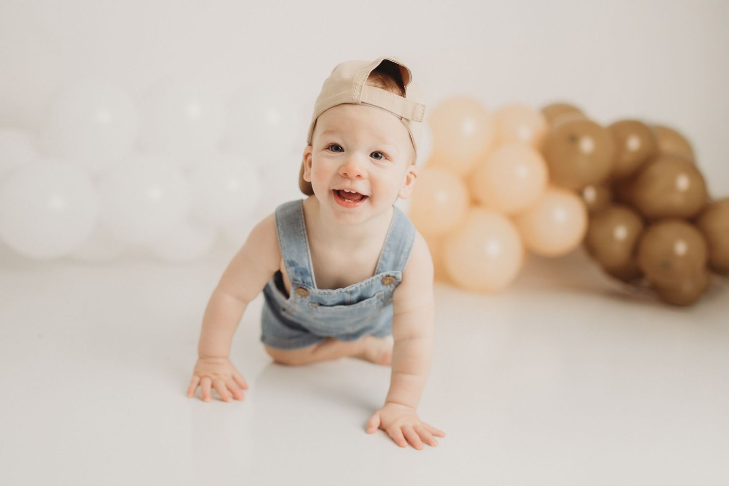 Baby in gray sweater lying on wooden surface with green and black balloons in background.