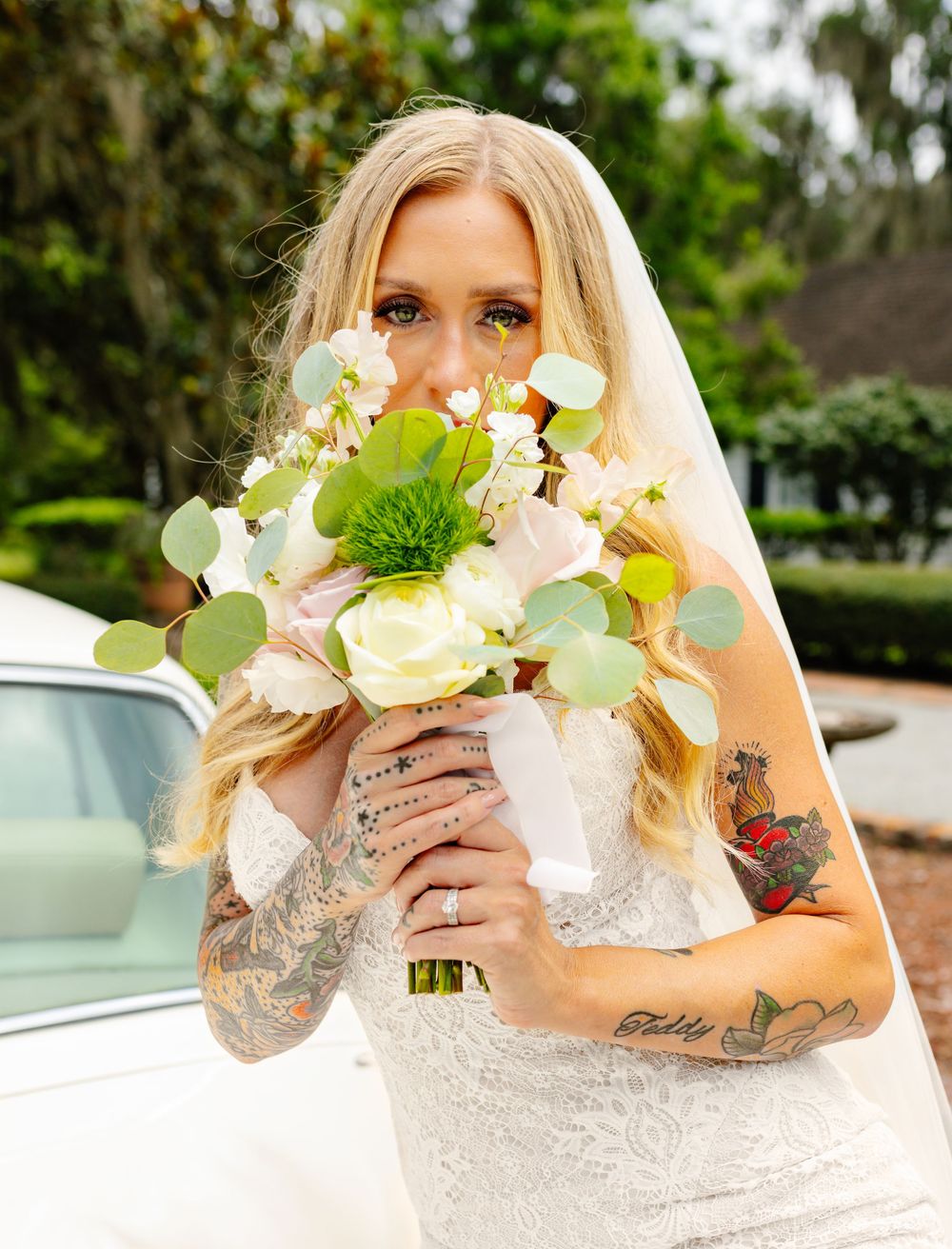Bride with tattoos holds elegant bouquet of white roses and green eucalyptus.