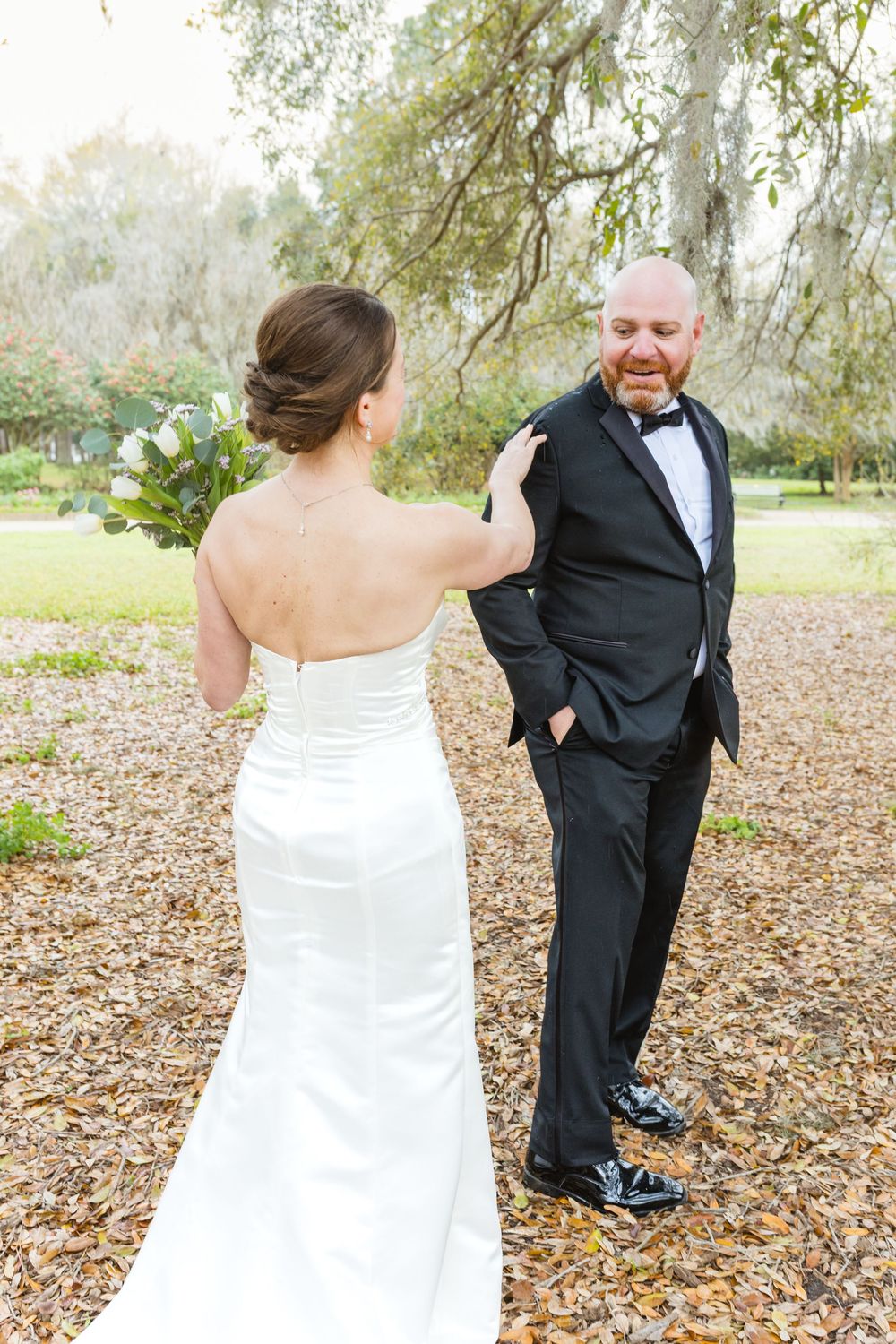Playful wedding couple interacts on fallen leaves during their outdoor photo session.