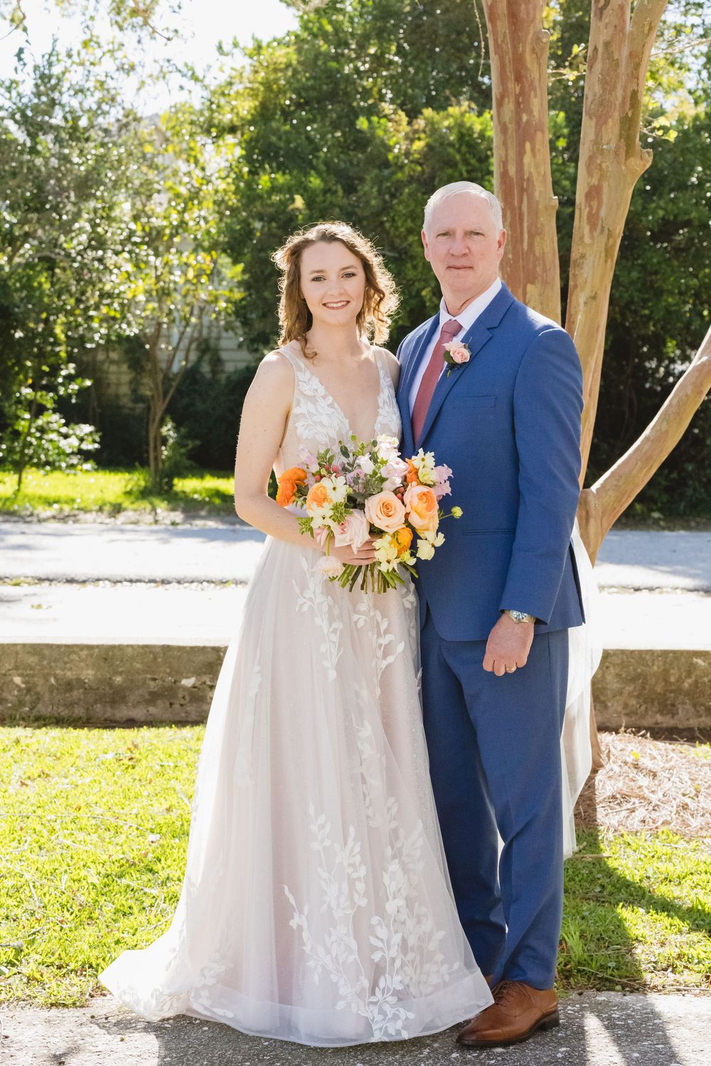 Couple poses for wedding photos outdoors with bright sunlight filtering through trees.