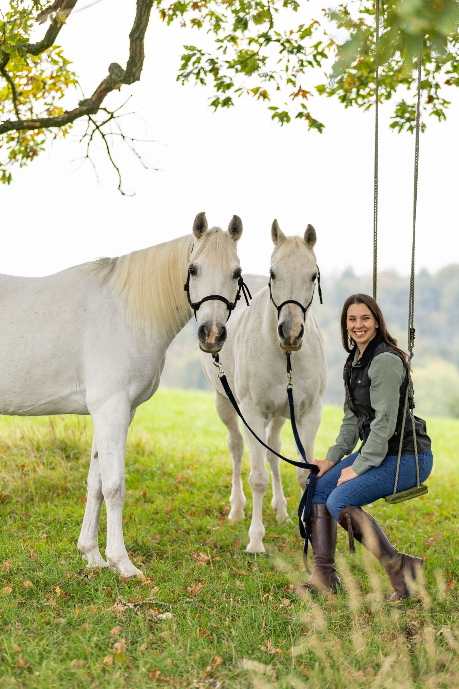 A group poses with horses along a tree-lined path during a sunny autumn day for outdoor photos.