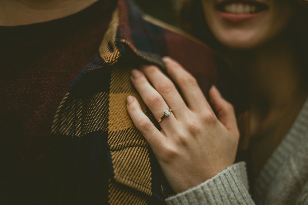 A person wearing a cozy gray sweater holds a plaid scarf while wearing an engagement ring. Edmonton Engagement Photographer