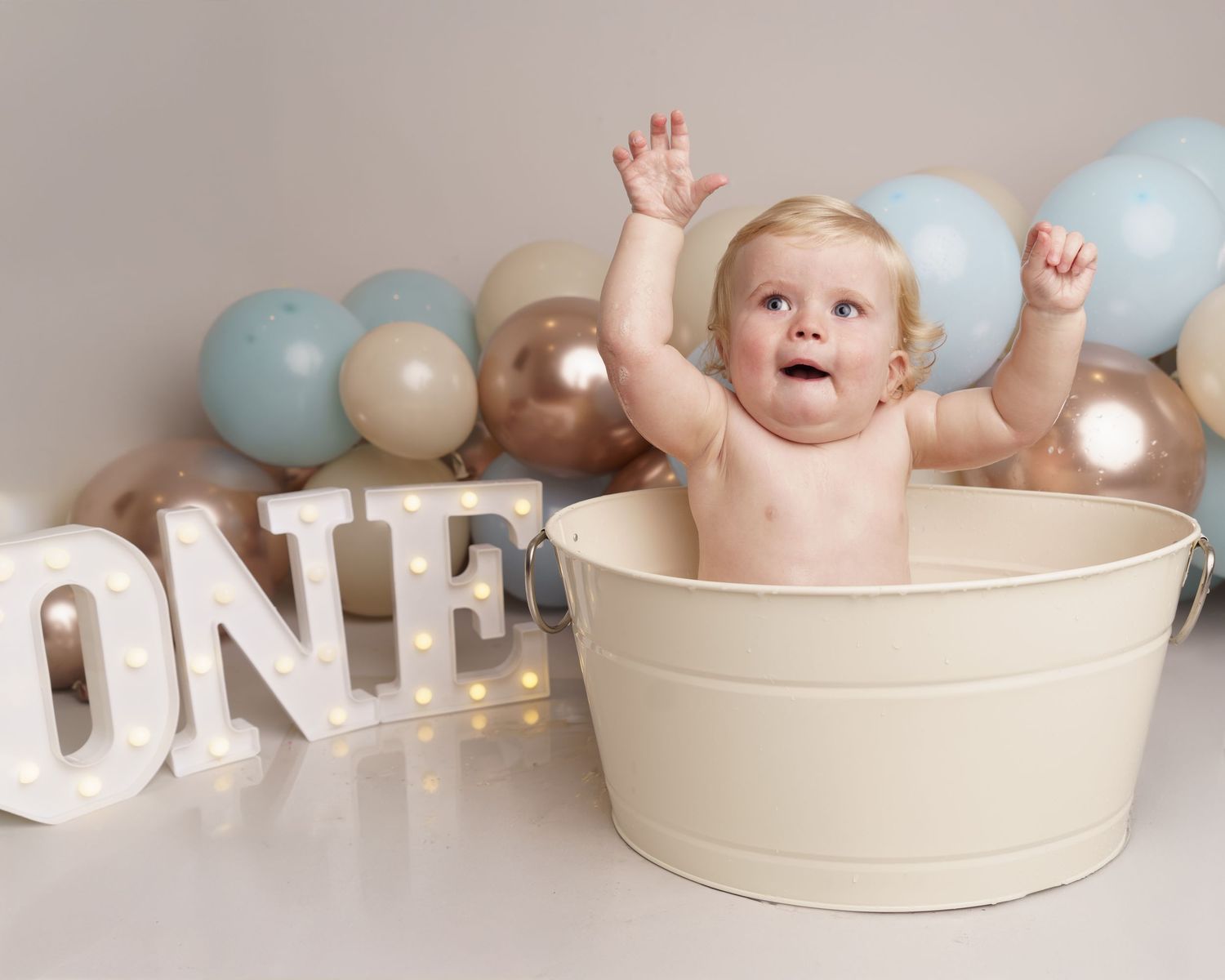 First birthday celebration scene with pale blue and gold balloons and illuminated 'ONE' letters.