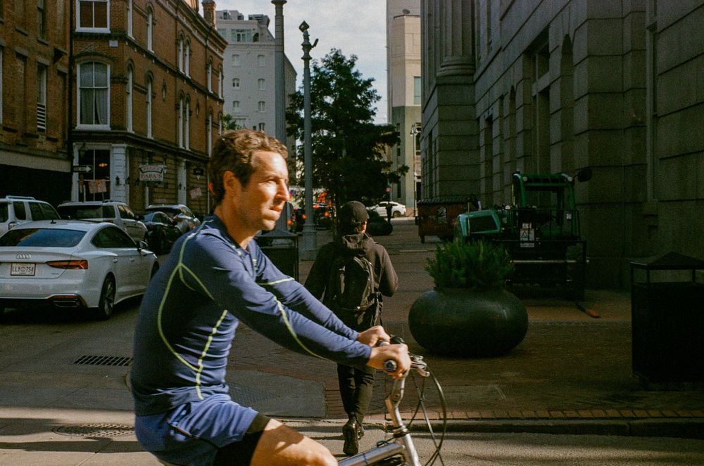 Cyclist in blue outfit rides through city street with buildings in background.