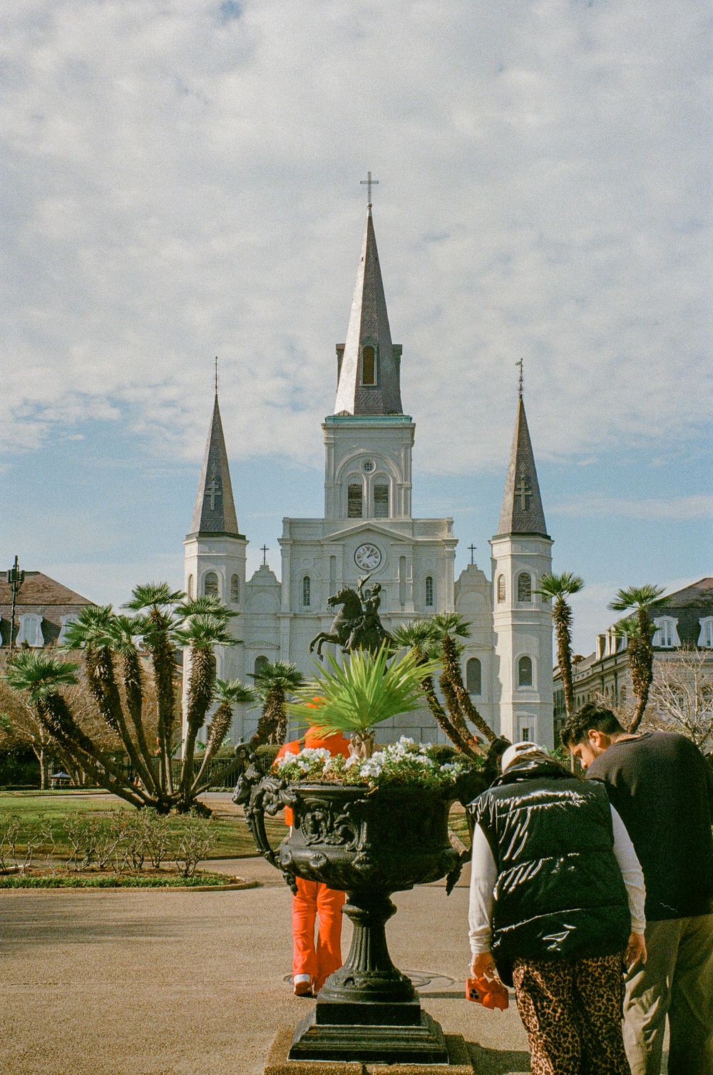 Historic St. Louis Cathedral in New Orleans with white spires against cloudy sky and tropical plants.