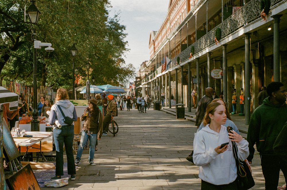 Bustling street scene with shops, outdoor dining, and pedestrians walking along tree-lined sidewalk.