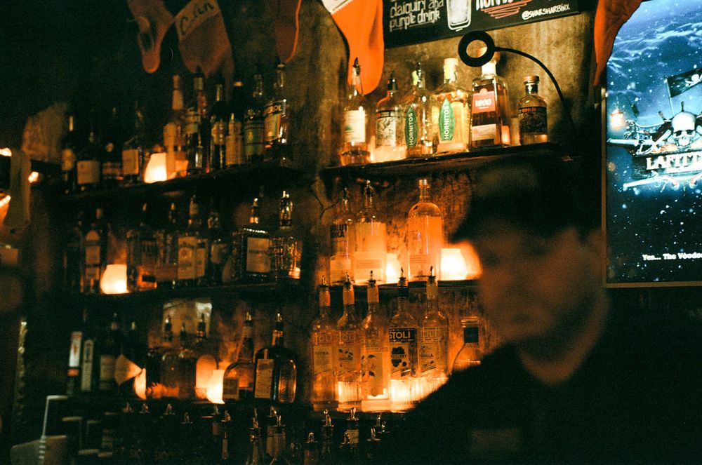 Dimly lit bar interior with shelves of bottles illuminated by warm ambient lighting.