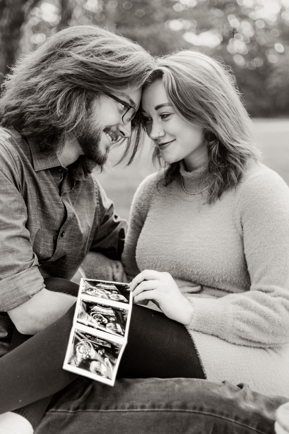 Couple shares an intimate moment while looking at ultrasound photos together in black and white.