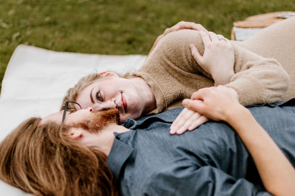 Couple shares joyful laughter while lying together on picnic blanket outdoors.