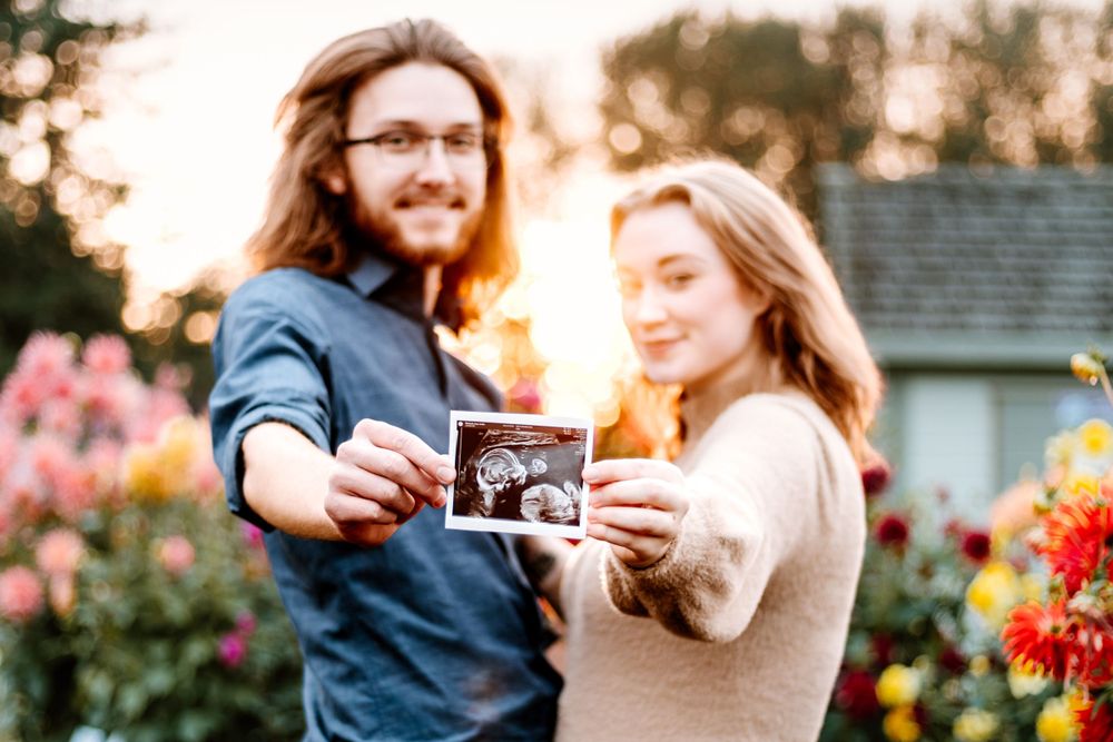Couple holding ultrasound photo together in garden during sunset.