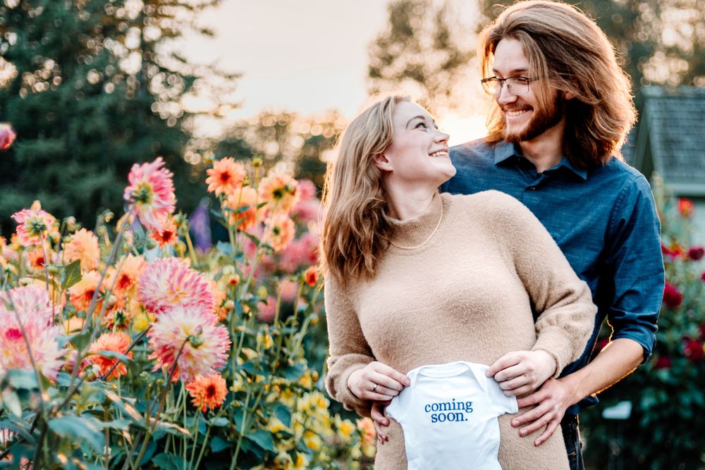 Couple shares tender moment in garden while holding baby onesie.