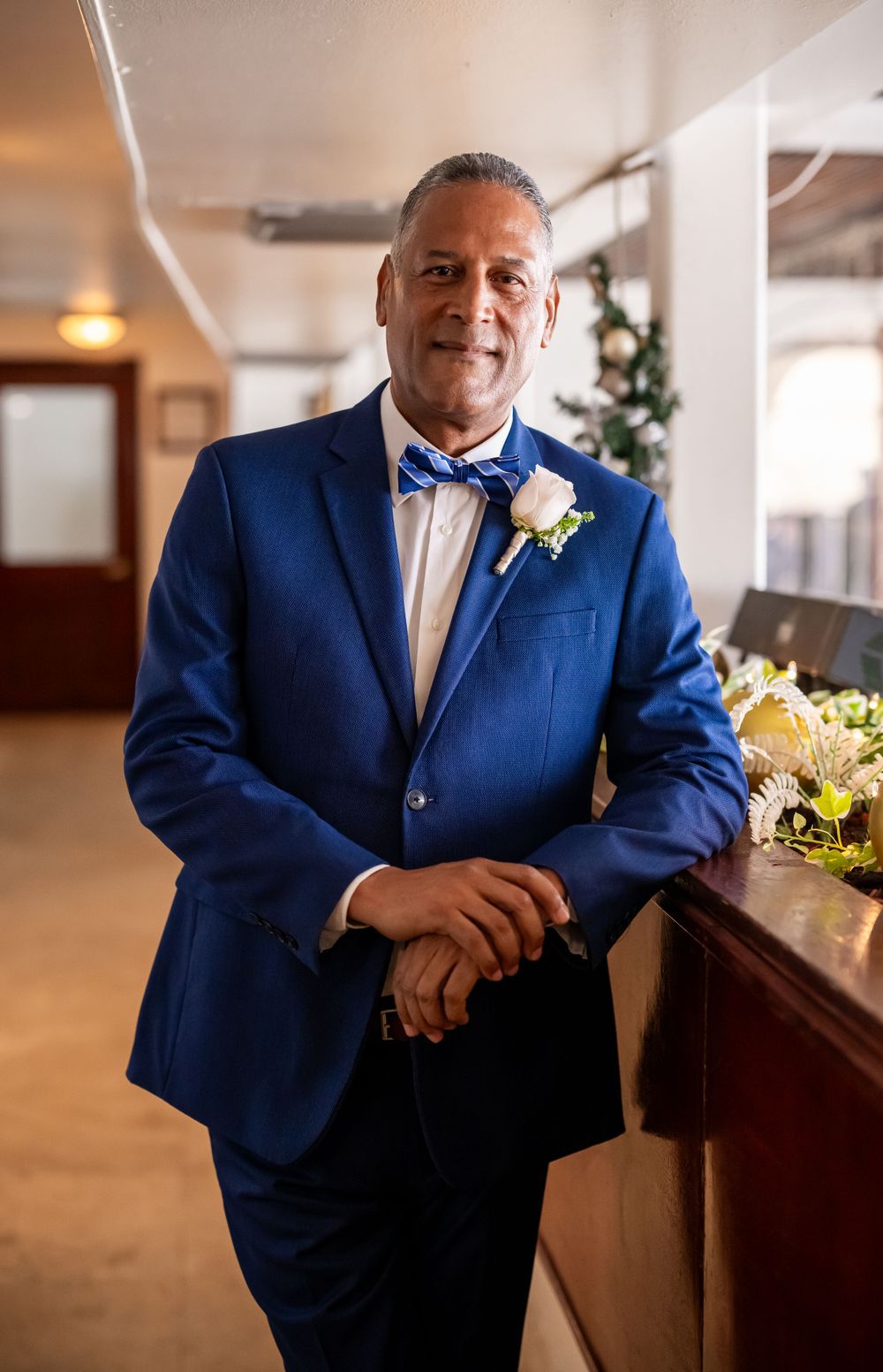 A confident groom in a navy suit and bowtie stands beside decorative flowers.