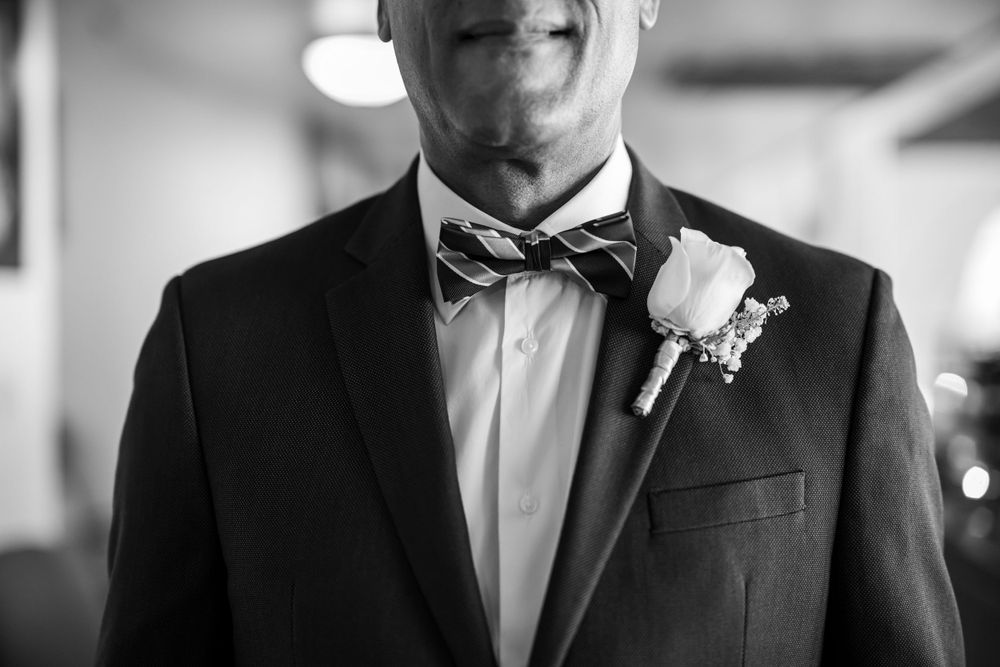 Black and white detail shot of a groom wearing a classic tuxedo with bowtie and boutonniere.