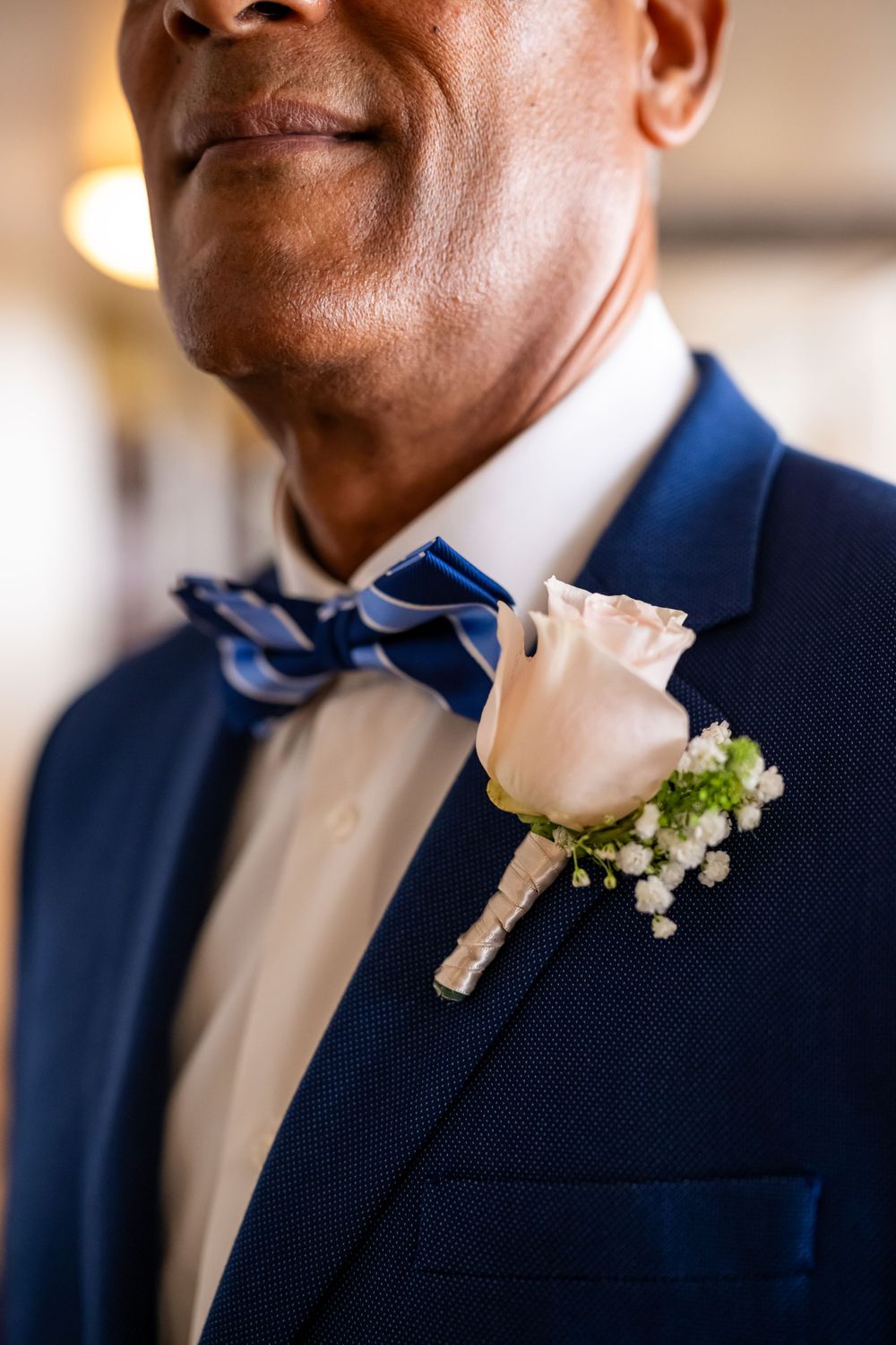 Close-up detail of a navy suit with striped bowtie and white rose boutonniere.