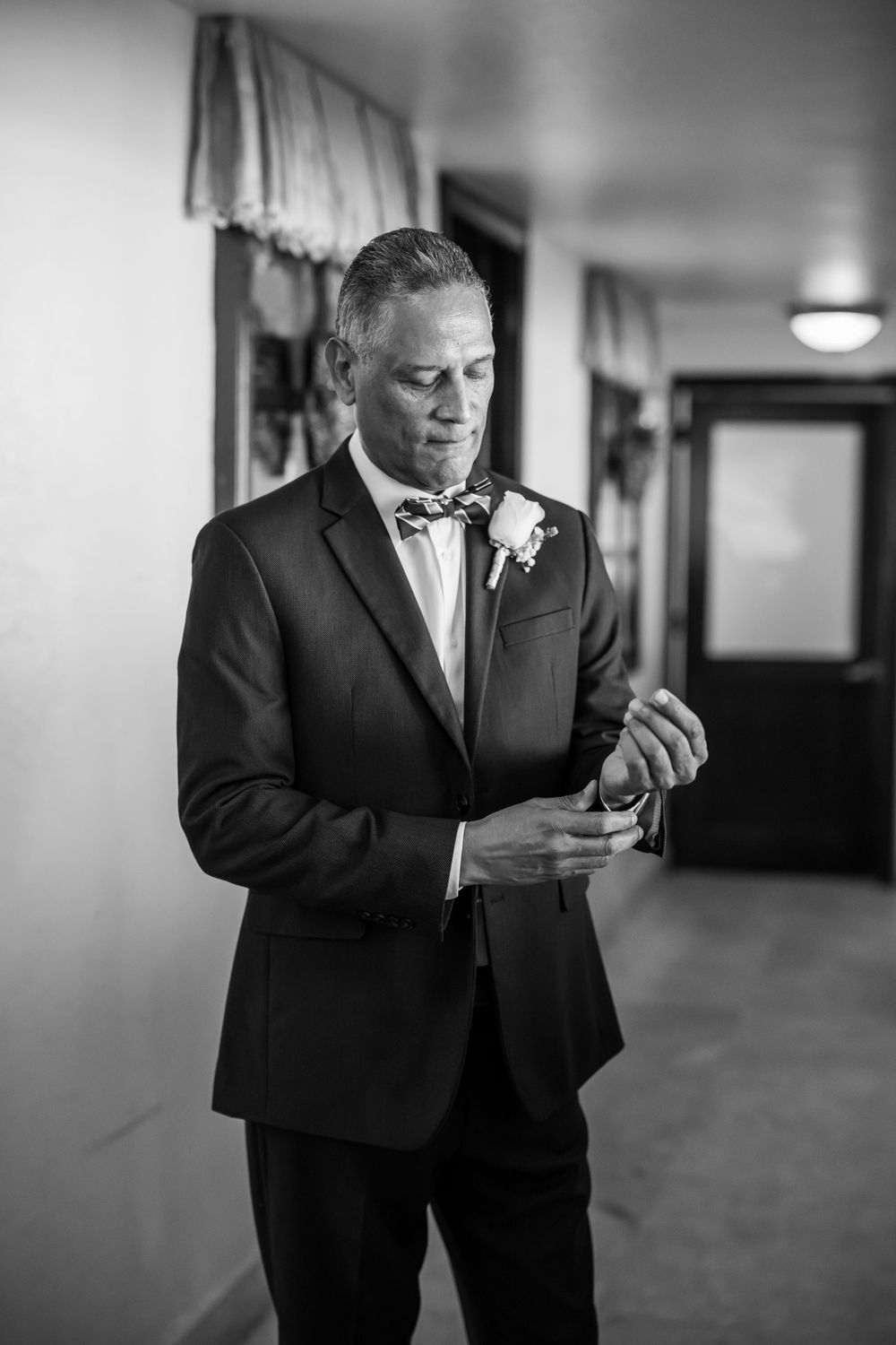 A groom in a black tuxedo and bow tie checks his watch while getting ready for the wedding ceremony.