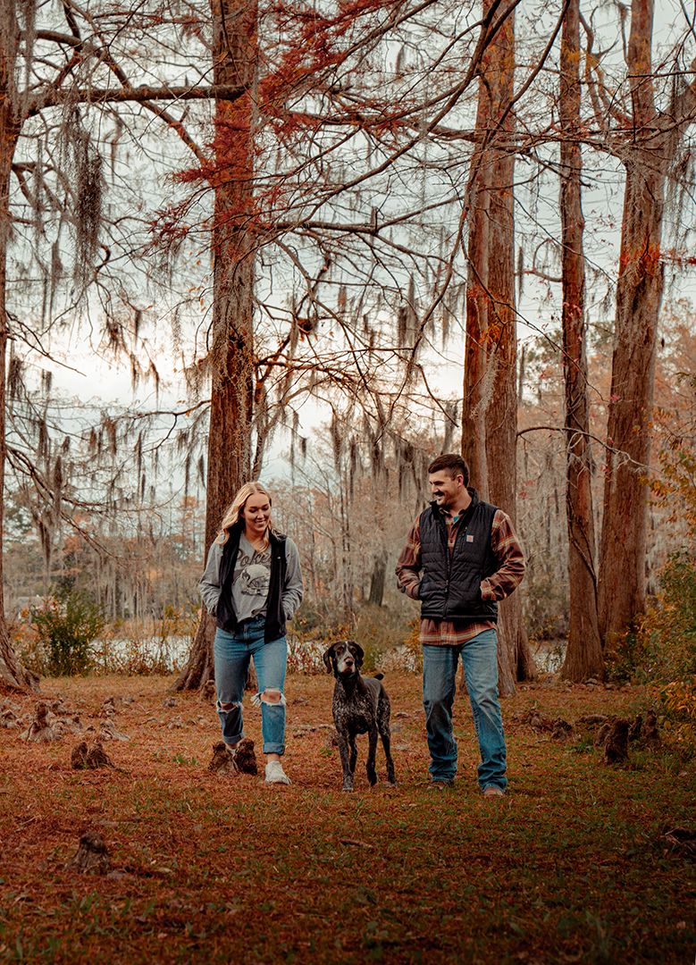 A couple walks their black dog Jeb through an autumn forest with Spanish moss hanging from trees at Greenfield Lake.