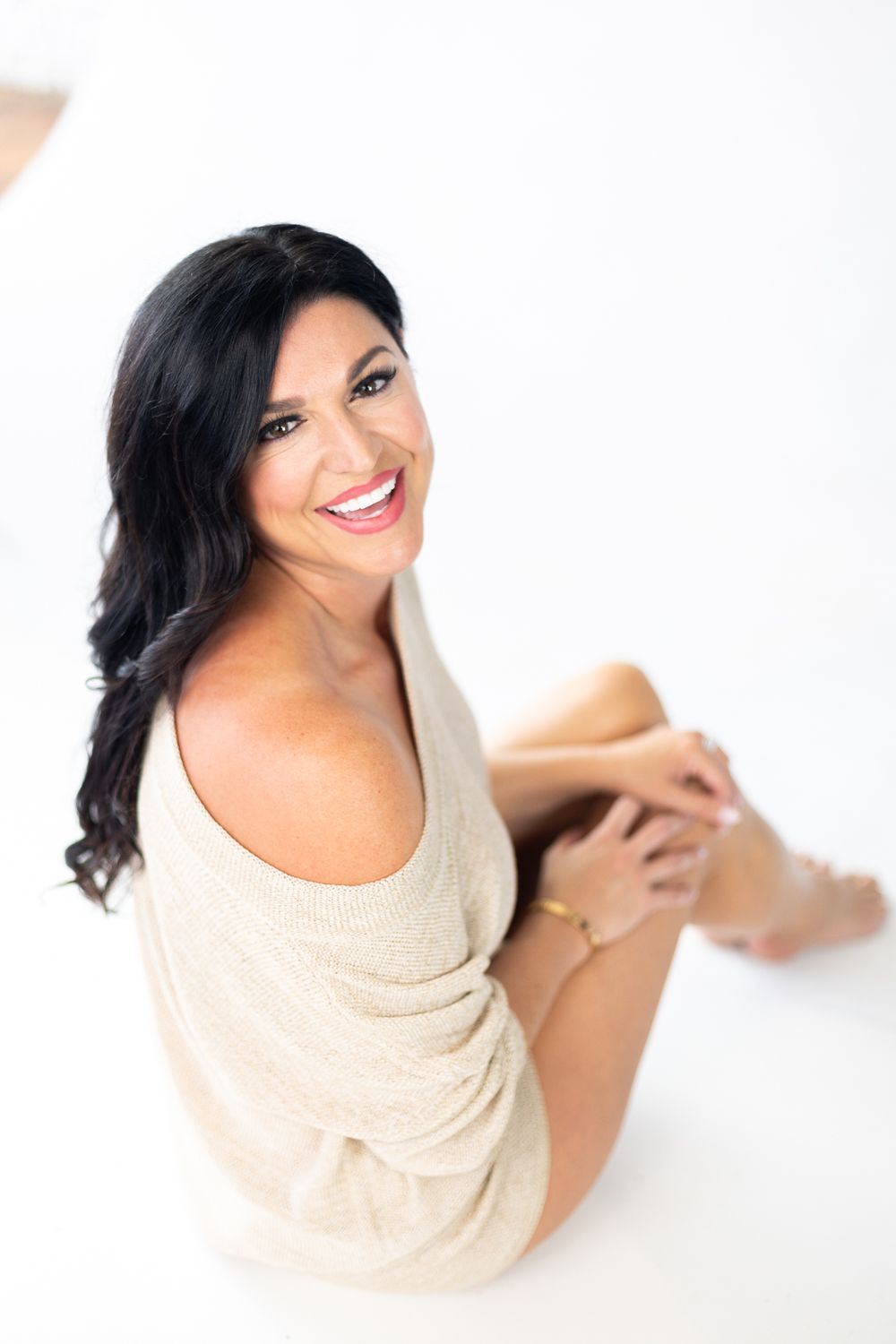 Woman wearing beige sweater poses cheerfully on white background in casual portrait session.