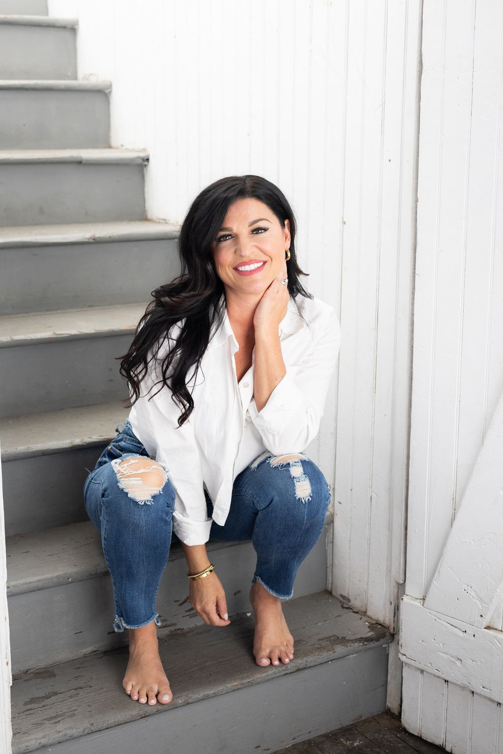Candid portrait of woman in white shirt and ripped jeans sitting on grey stairs.