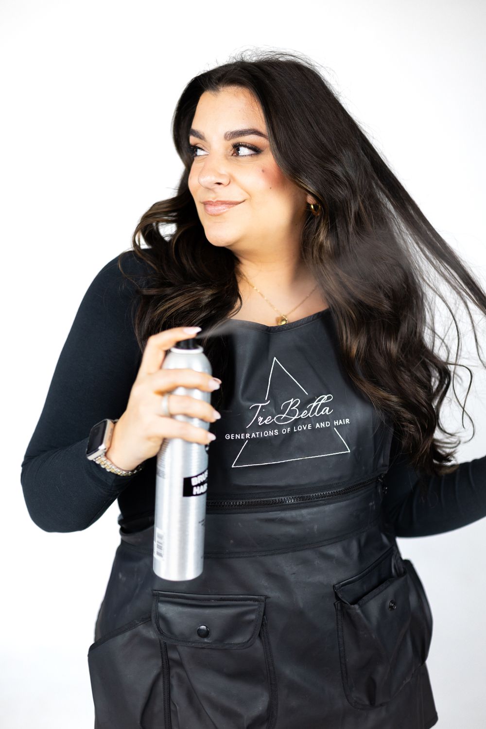 A woman in black clothing holds a spray bottle against a white background.