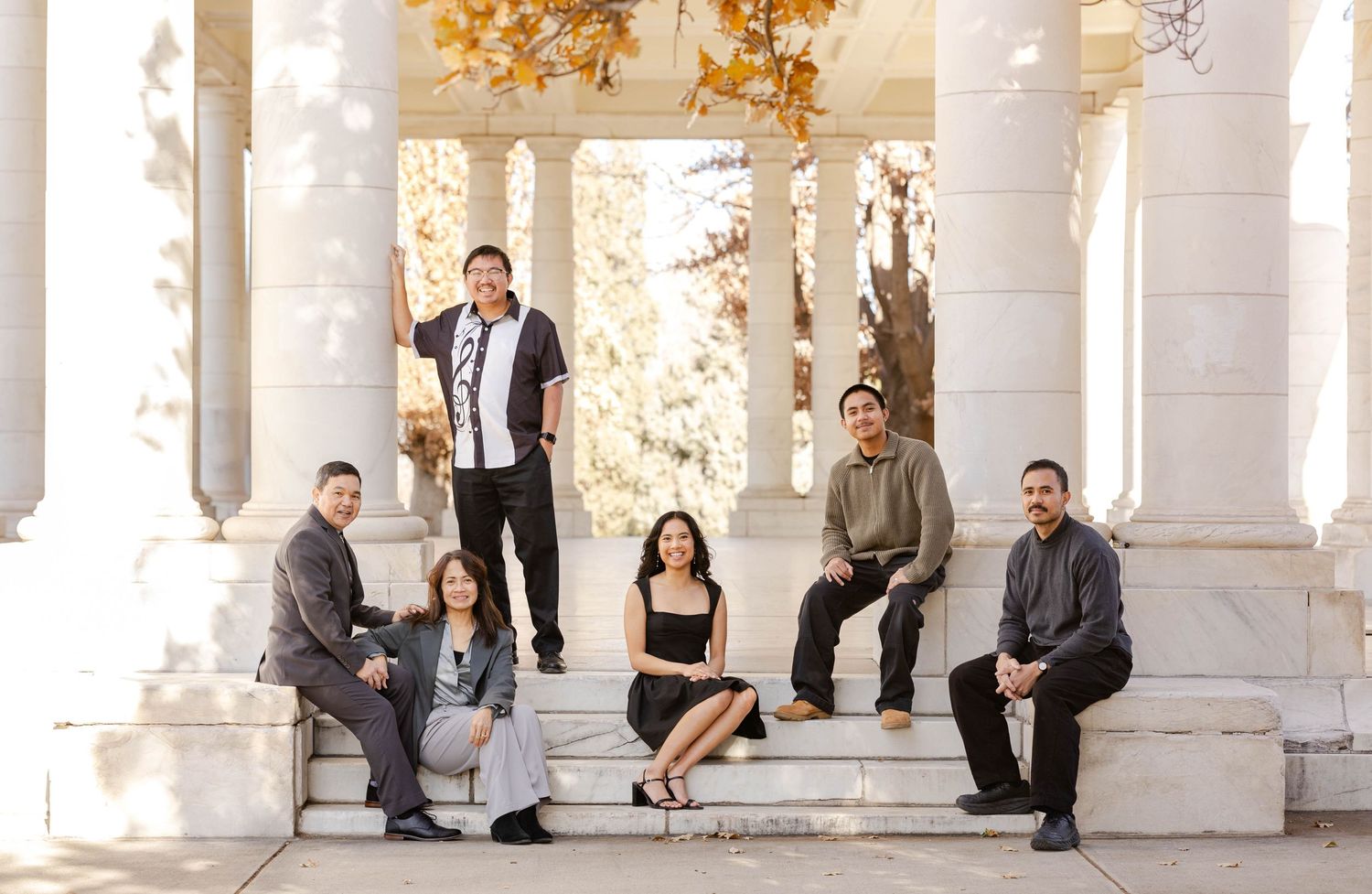 Group poses casually on white columned porch steps during outdoor photo session.