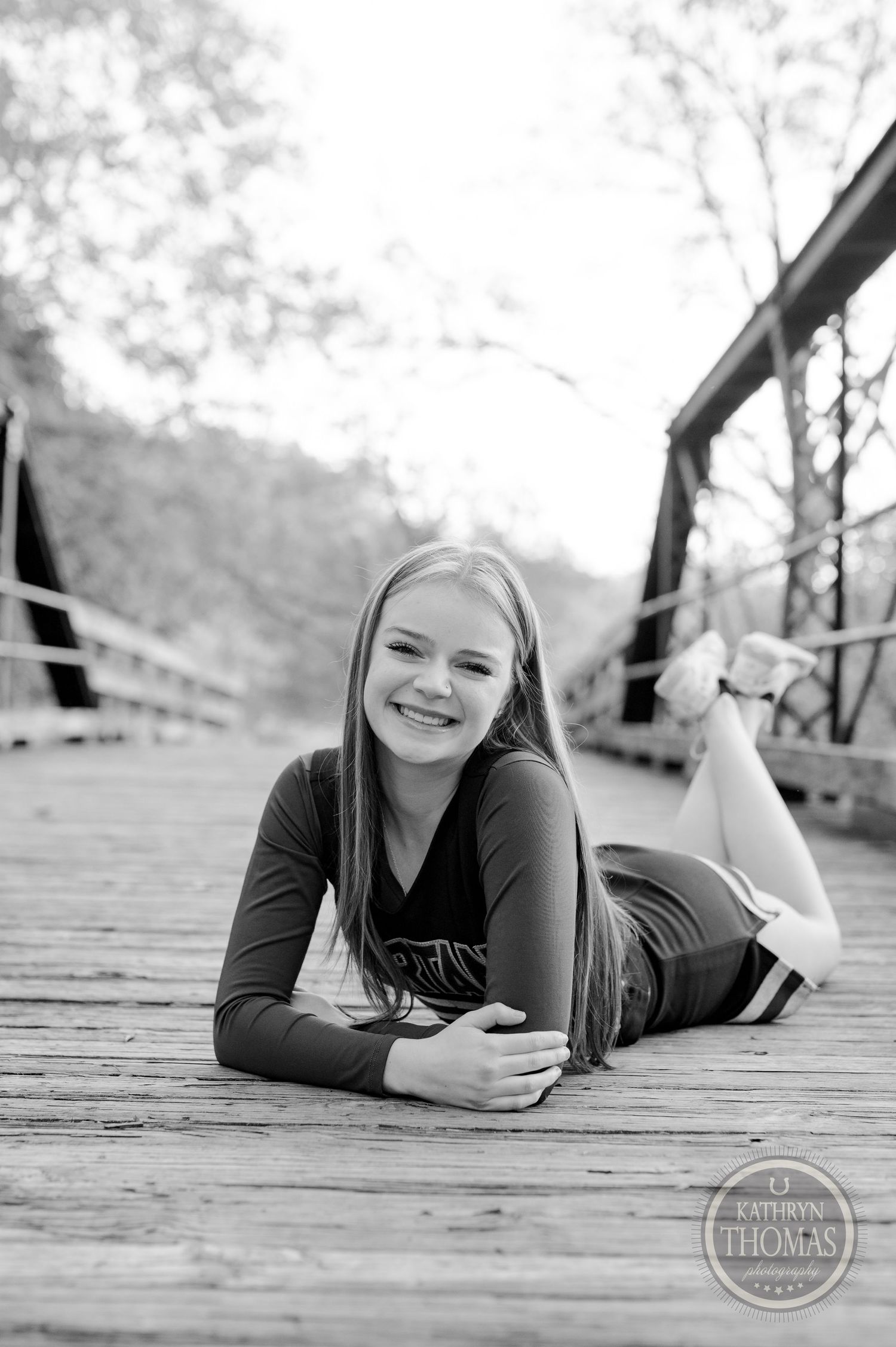 Black and white portrait of cheerleader lying on wooden bridge in casual pose.