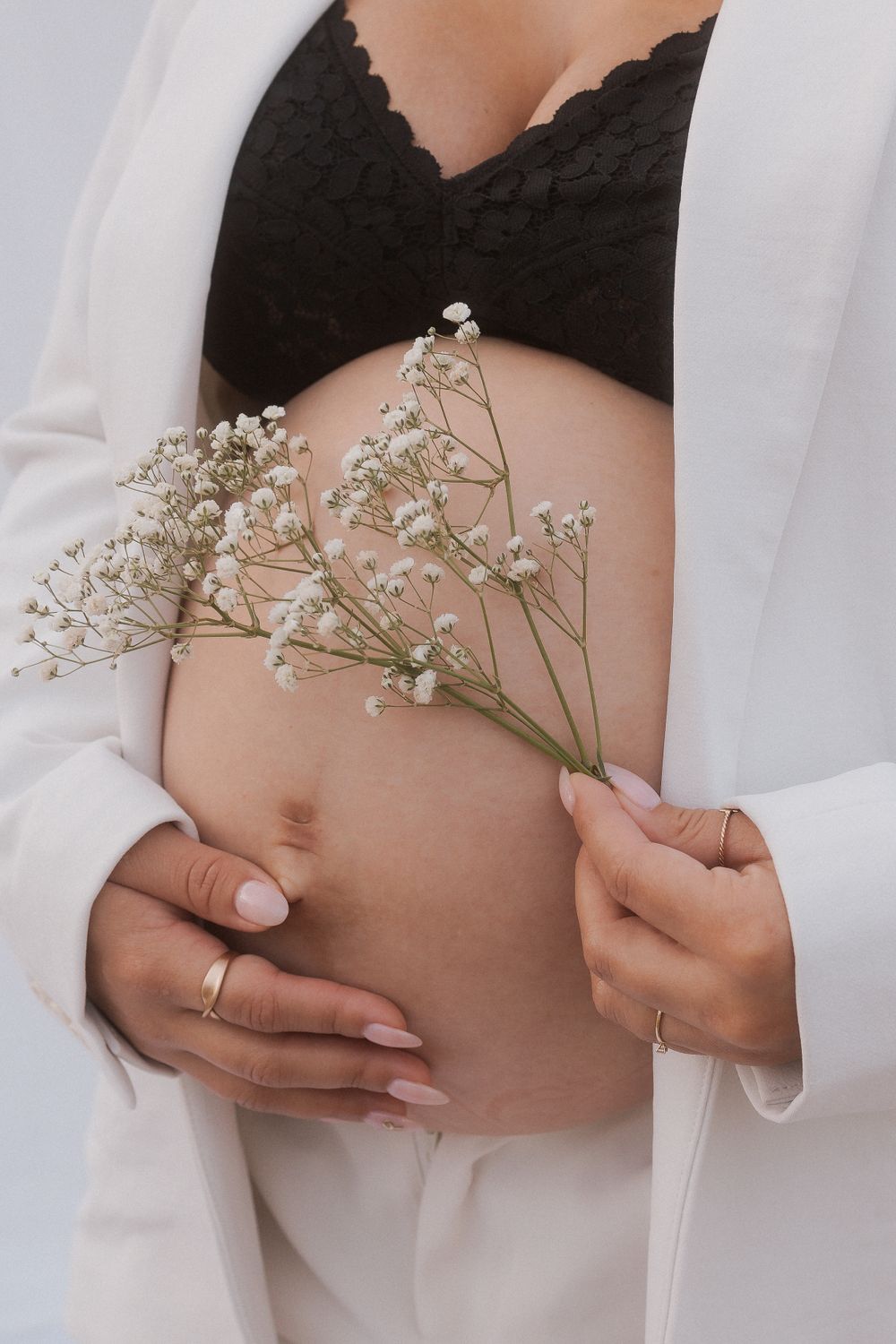 Delicate baby's breath flowers held against pregnant belly with white blazer and black lace top.