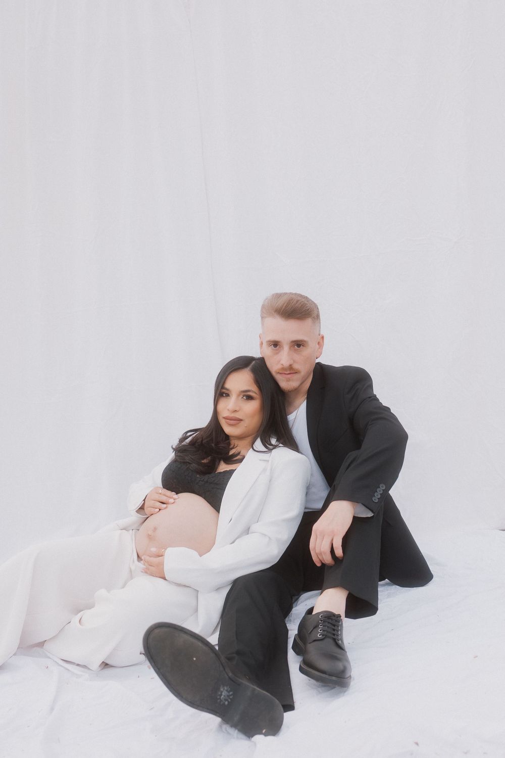 Intimate maternity studio portrait with couple on white background.