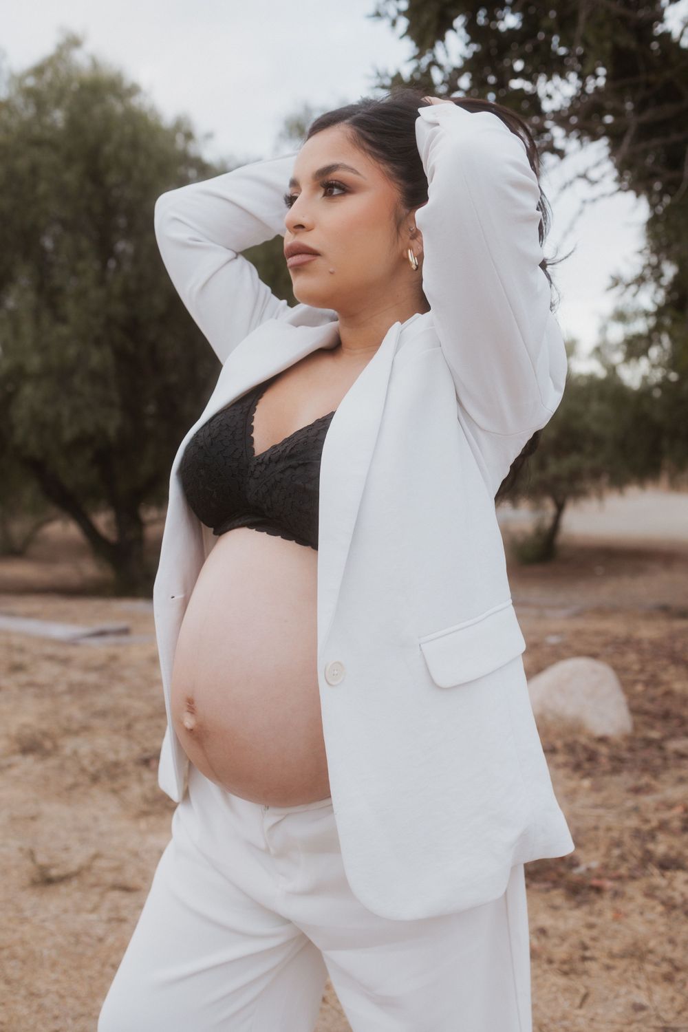 Stylish maternity pose showcasing pregnant belly in white blazer against outdoor setting.