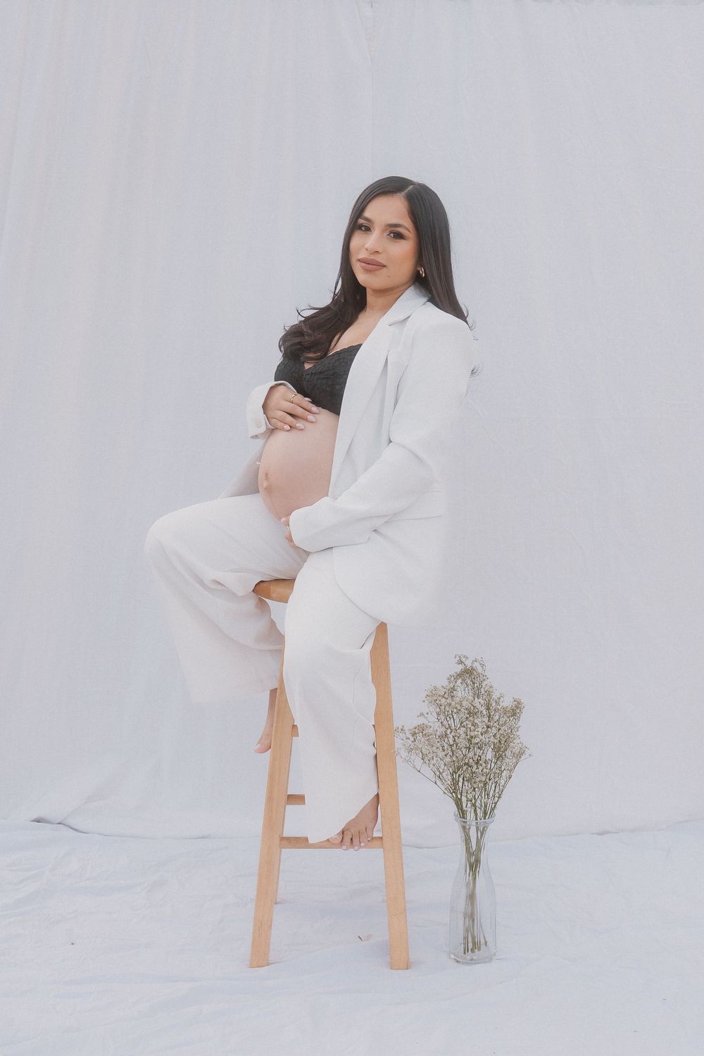 Elegant maternity portrait of expectant mother in white suit on wooden stool.
