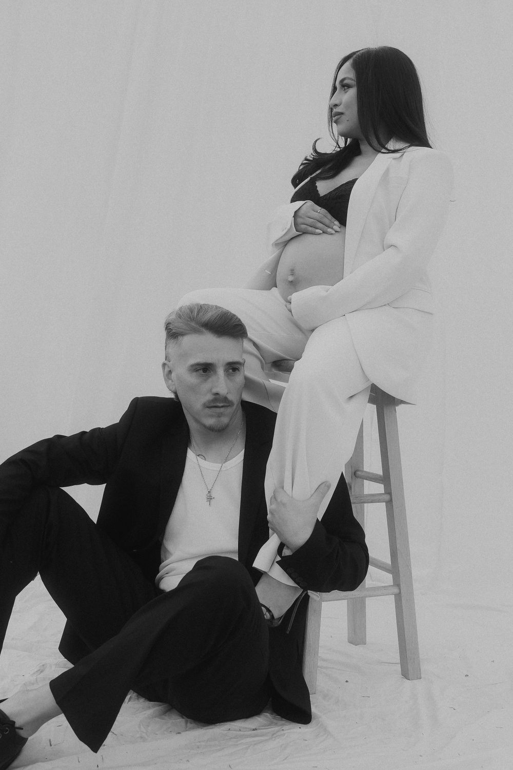 Artistic black and white maternity portrait with couple against plain background.