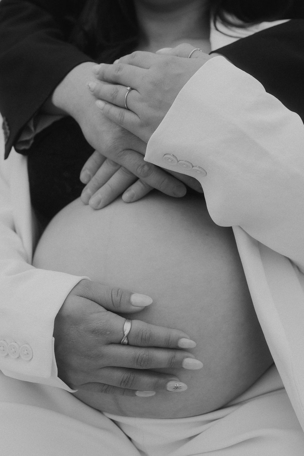 Close up of hands with wedding rings resting on pregnant belly in black and white.