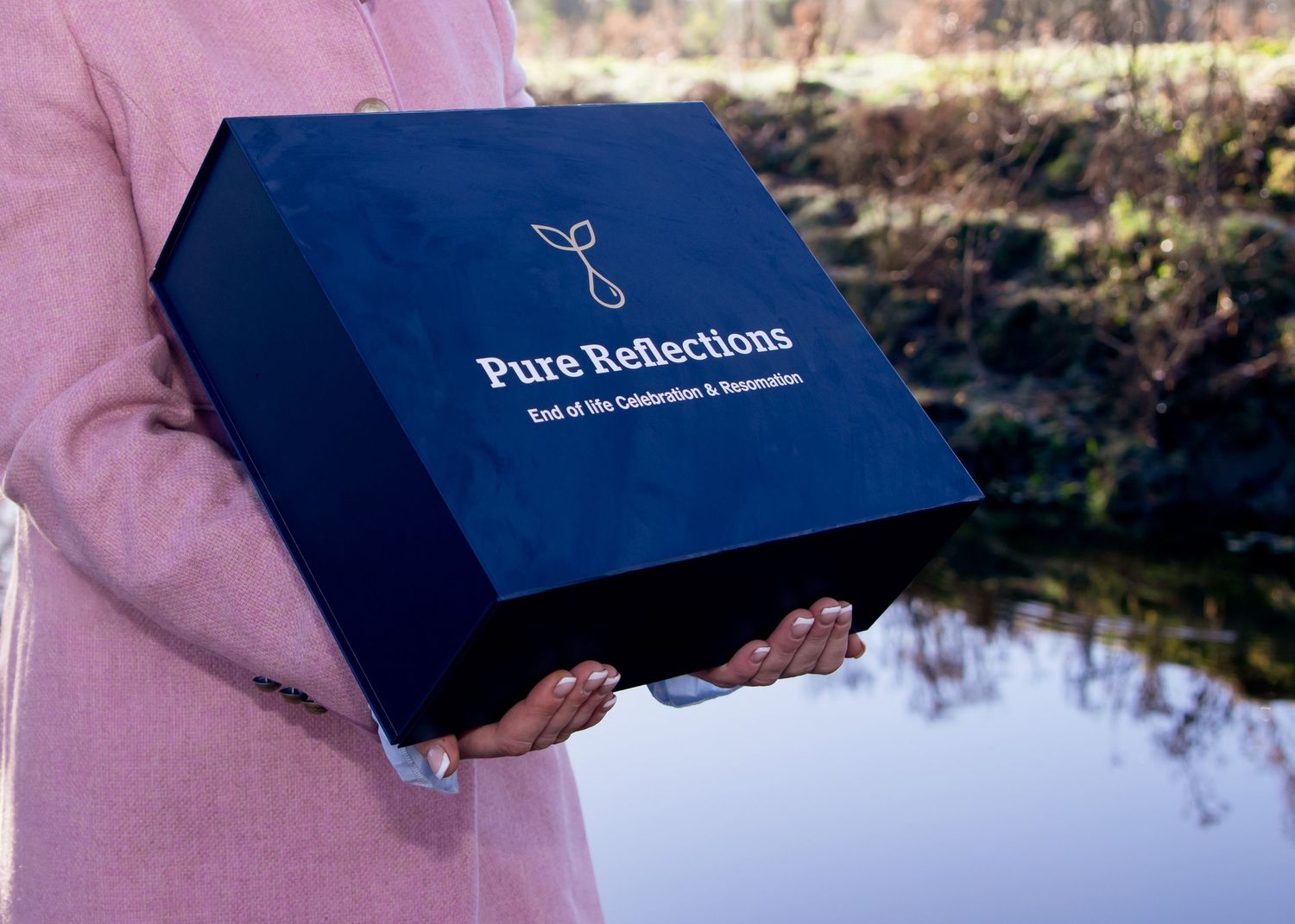 Close up of navy blue box with gold text being held outdoors.