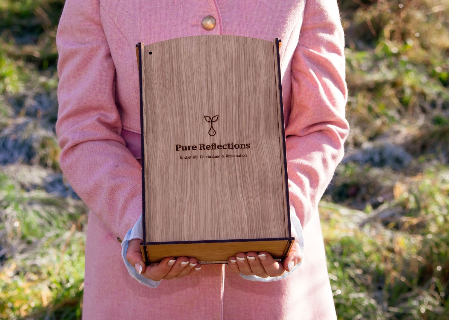 Wooden textured box with branding being displayed against pink clothing.