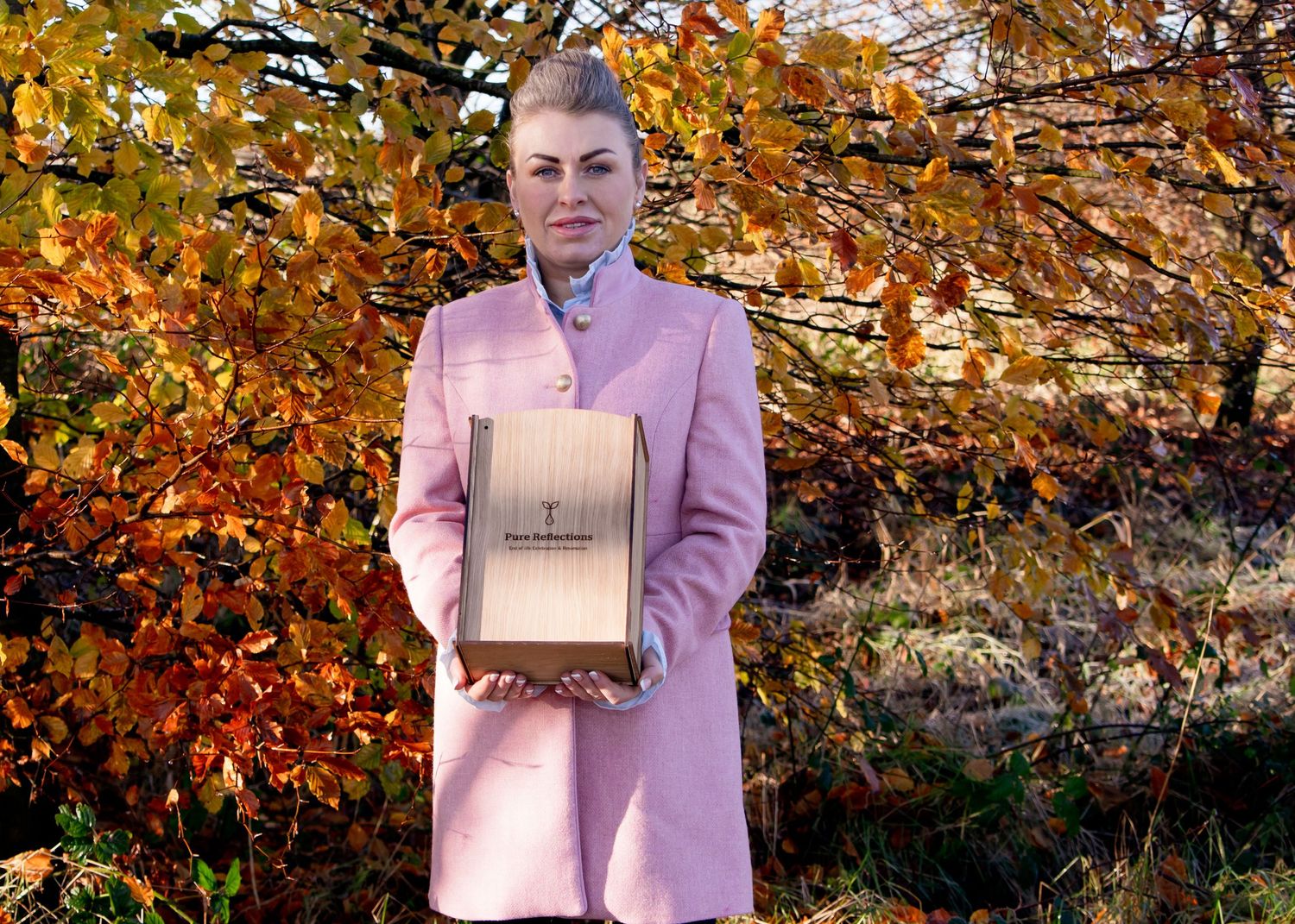 Person holding wooden box against autumn foliage background.