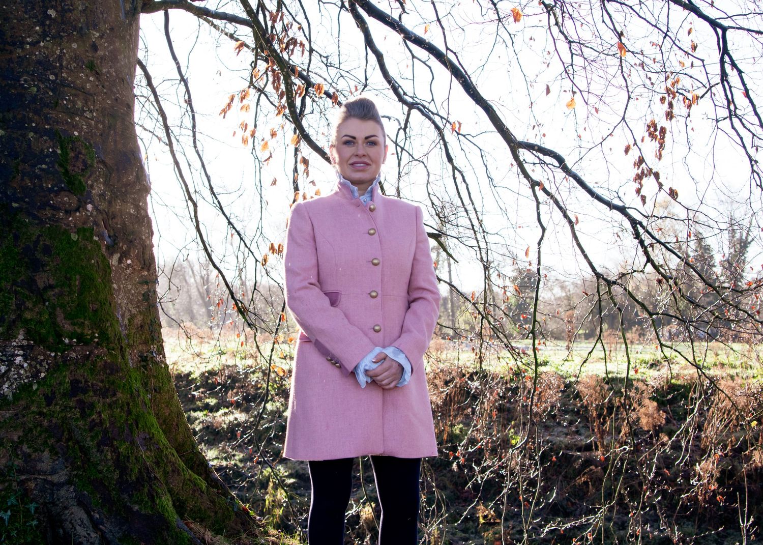 Person in pink coat standing near bare winter trees.